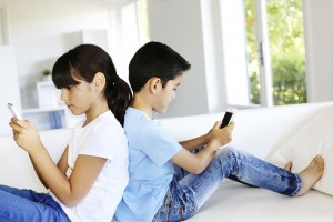 Two children sitting back to back and texting